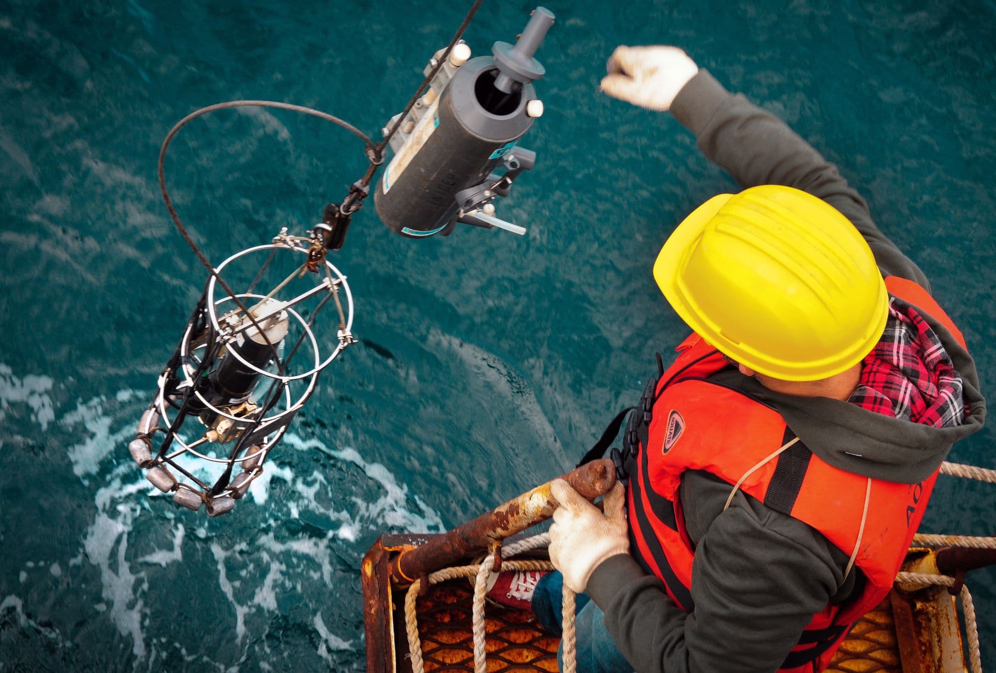 Offshore worker in hard hat and life vest guiding equipment over the side of a vessel
